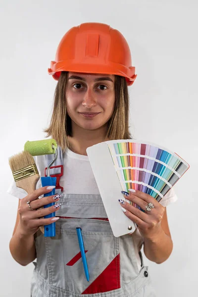 Yüzünde mutlu bir ifadeyle kameraya bakan kasketli kadın inşaat işçisi. Kadın tulum ve koruyucu bir kask giymiş. tipik bir arkaplanda izole edilmiş.