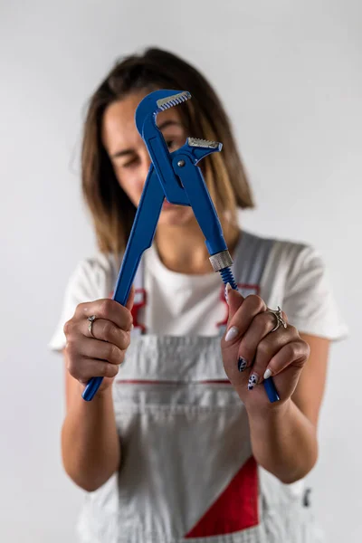 beautiful young woman in suspenders holds a blue wrench in her hands. portrait of a woman in uniform. isolated on white background.