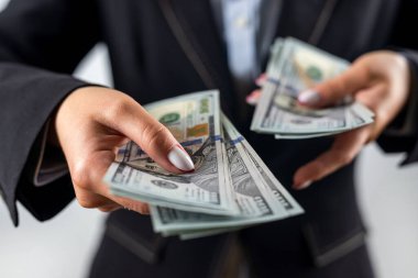 Siyah ceketli, beyaz arka planda dolar banknotları olan güzel bir genç kadın. Dolarlar kadınların elinde. İş. kar.