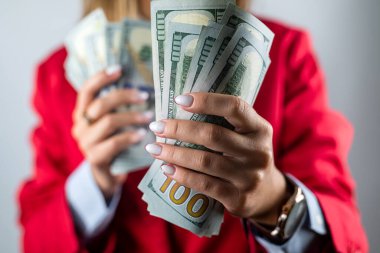 Kırmızı ceketli güzel genç bir kadın arka planda izole edilmiş bir yığın parayı dolarla gösteriyor. Para için. Dolarlar hazır.