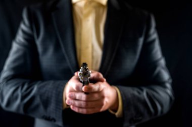 Gizli ajan olarak silah tutan takım elbiseli bir adam siyah bir arka planda izole edilmiş. Silahlı bir adam kavramı. Ellerinde tabanca, göğsünün önünde.