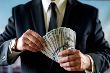 İş adamı bir aylık kazancını kendi ellerinde tutar. Para ve ticaret kavramı. Dolarla ellerini kapat.