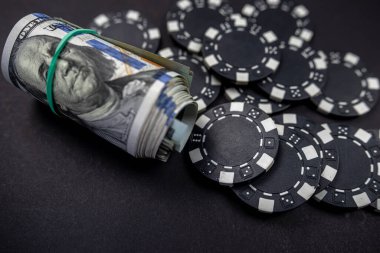 Siyah arka planda izole edilmiş bir rulo Amerikan dolarıyla saçılmış renkli poker fişleri. Kumar oynuyorum. poker