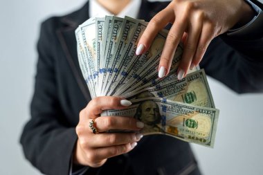 Tarz sahibi siyah takım elbiseli neşeli genç bir kadın arka planda izole edilmiş dolarları tutuyor. İş kadını..