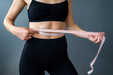 Yakın plan, eğitimli bir mideyi mezurayla ölçüyor. Spor, spor ve diyet konsepti. Vücut boyutlarının ölçümü