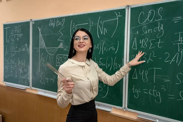 教室で黒板に数式を書いている若い女性は — ストック写真
