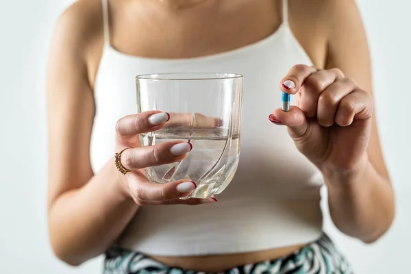 woman takes cosmetic supplements for glowing skin while holding fish oil capsules and a glass of water. isolated on white background. female hands capsule and water in a glass