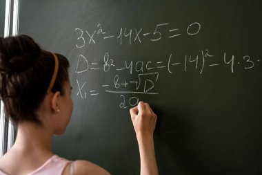 Matematiksel formülleri ve eğitim kavramını tamamlayan karatahtaya yazı yazan zeki bir kız öğrenci. 