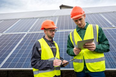 Güneş panellerini inceledikten sonra özel kasklı iki genç adam not alıyor. Yeşil enerji tasarrufu kavramı