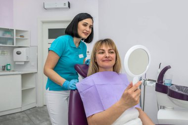 beautiful young patient looks in the mirror near the dentist evaluating his work. Healthy smile concept