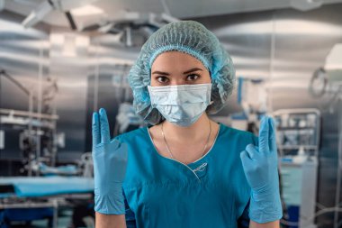 Mavi ceketli doktor ya da hemşire mavi lastik eldiven giyer ve bir hastayı ameliyathanede muayene etmeye hazırlanır. İlaç. Ameliyathane doktoru