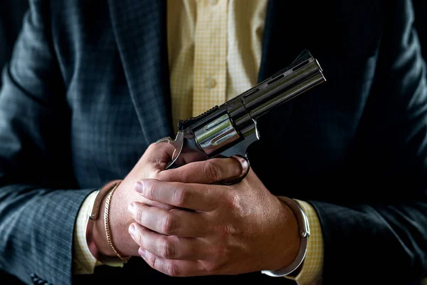 man in a tuxedo and shirt without a face holds a revolver in his hands near his chest isolated on a black background. male hands with a gun. hands in front of the chest with a revolver