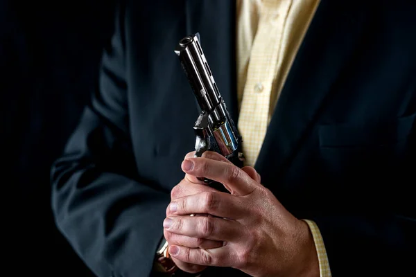 man in a suit holding a gun as a secret agent isolated on a black background. The concept of a man with a gun. hands with a revolver in front of the chest