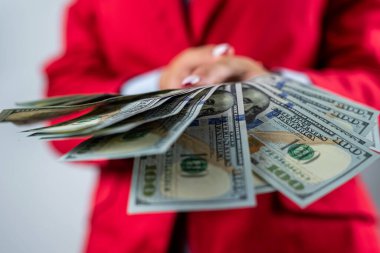 Kırmızı ceketli güzel genç bir kadın arka planda izole edilmiş bir yığın parayı dolarla gösteriyor. Para için. Dolarlar hazır.
