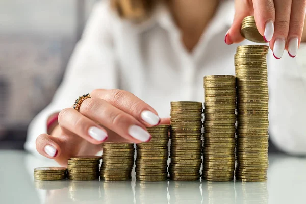 hands of a business woman taking several coins from a coin slide on a glass and modern office table. sense of tax or make money. Investment in business and maintaining growth for advertising concept.
