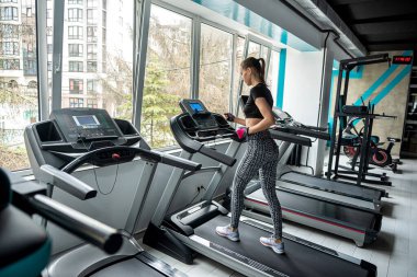 Genç bayan antrenör hayallerini gerçekleştirmek için spor salonunda çalışıyor. Kaslı vücutlu çekici bir kadın modern, parlak bir spor salonunda çalışıyor. Tatbikatlar yapılıyor.