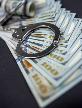 Polis kelepçeleri siyah arka planda izole edilmiş bir sürü doların üzerinde yatıyor. Suç. Adalet ve para. Kelepçeli suç ve yolsuzluk kavramı.