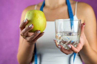 Kadın, beyaz bir arka planda izole bir şekilde kilo vermek için elma ya da su seçmeden önce ayakta duruyor. Diyet konsepti. Sağlık