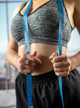 Genç, güzel bir kadın, spor salonunda panoramik pencereli bir mezura ile mükemmel ince bir vücut ölçüsü veriyor. Diyet Sağlıklı Yaşam Tarzı. fitness