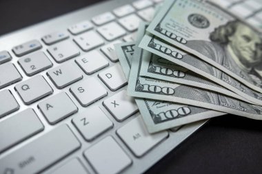 Beyaz bir dizüstü bilgisayarda yığınla Amerikan doları. Yukarıdan bak. Ücretli ofis işi