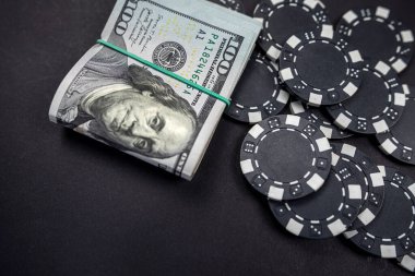 Siyah arka planda izole edilmiş bir rulo Amerikan dolarıyla saçılmış renkli poker fişleri. Kumar oynuyorum. poker