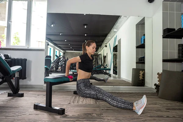 young female trainer works out in the gym to get the figure of her dreams. An attractive woman with a muscular body is working out in a bright modern gym. Performing exercises.