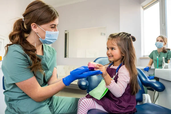 A small child at a dentist\'s appointment, the doctor shows and tells how to brush your teeth on artificial jaws