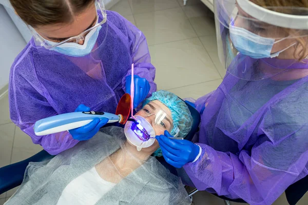 the dentist with his assistant in overalls uses UV lamps, then treats patients' teeth. Tooth restoration concept
