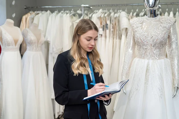 female seller hold pen and notes near wedding dress in boutique. Wedding day