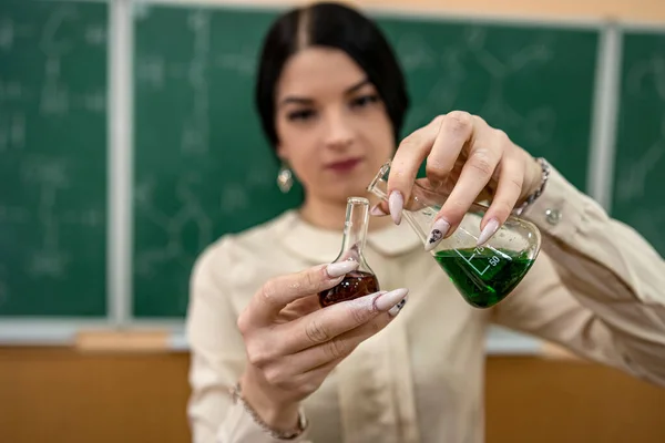 beautiful young female student is practicing in a chemistry classroom with flasks on the background of a board with formulas. Chemistry concept