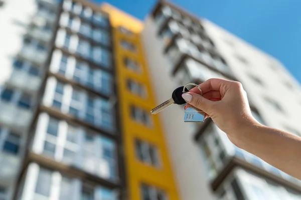 Evin anahtarı, yeni bir apartmanın arka planına karşı bir kadının elinde. Emlak kavramı