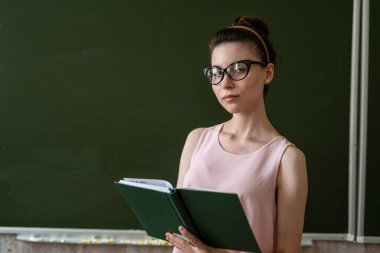 Güzel genç bayan öğretmen veya öğrenci boş tahtanın yanında duruyor.