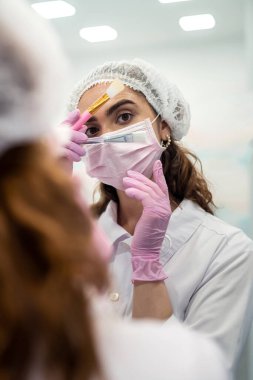 Aynanın yanında maske takmak için kemikleri olan bir güzellik uzmanı. Kozmetoloji prosedürleri kavramı. güzellik küresi