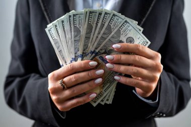 Siyah ceketli, beyaz arka planda dolar banknotları olan güzel bir genç kadın. Dolarlar kadınların elinde. İş. kar.
