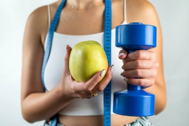 Elinde mavi dambıl ve elma tutan, elinde mezura olan zayıf, tanınmayan bir kadın. Kilo kaybı ve sağlıklı yaşam tarzı kavramı.