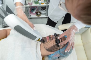 Bir müşterinin yüzüne sentetik fırçayla kil maske takan bir dermatoloğun yakın plan görüntüsü. Dermatolog kozmetoloji cilt sorunları