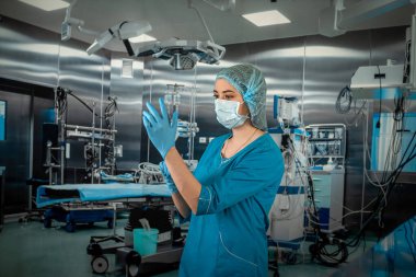 Mavi ceketli doktor ya da hemşire mavi lastik eldiven giyer ve bir hastayı ameliyathanede muayene etmeye hazırlanır. İlaç. Ameliyathane doktoru