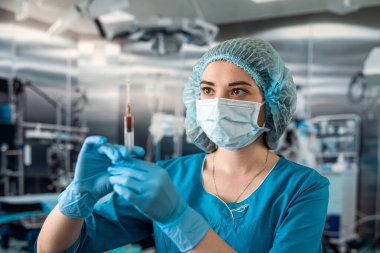 Maskeli ve eldivenli genç bir hemşirenin portresi elinde şırıngayla ameliyatta bir hastayı bekliyor. İlaç. hastaların bal odası tedavisi