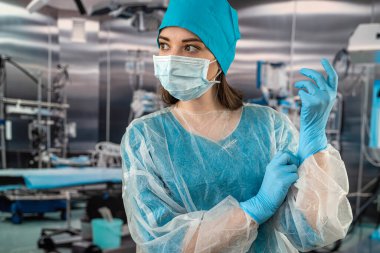 Bir kadın hemşire, karmaşık bir ameliyat sırasında kauçuk lateks mavi eldiven giyerken maske takan mavi bir üniforma giyer. İlaç. Doktorlar ameliyathane