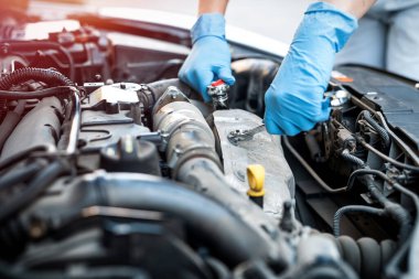 Araba tamirhanesinde, gülümseyen genç bir kadın tamircinin ellerini kapatıyorlar. Kadın tamirci. Kadın elleri kaputun altında.