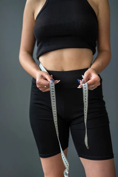 Young smiling beautiful woman measuring her ideal waist with tape measure isolated on gray background. in the background is a woman in the studio. diets Healthy Lifestyle