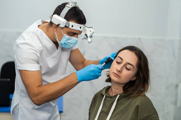 ENT doctor examines the ear with an otoscope of a female patient in the hospital. The doctor examines the patient's ear with an instrument.