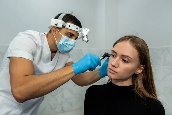 An otolaryngologist examines the auricle. Hearing clinic. An ENT doctor with instruments in a mask and gloves examines the patient\'s ear.