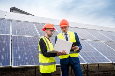 Büyük bir şirketin müdürü, özel giysili güneş panelleri takan bir çalışanın çalışmalarını inceliyor. Yeşil elektrik tasarrufu kavramı