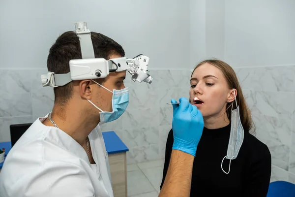 Doctor using an inspection spatula to examine the throat of a woman patient. An ENT doctor examines a woman\'s throat. the patient opened his mouth to examine the throat