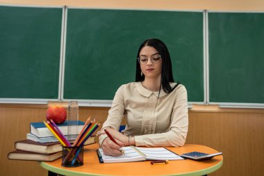 Kadın öğretmen kitap ve defterlerle bir masada oturur, konsept çalışır.