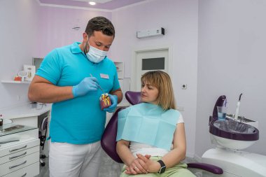 Diş kliniğinde asistanı ve hastası olan mutlu bir kadın diş hekimi bir sorun dişini inceliyor. Dişçi konsepti. Ağız boşluğunun temizliği ve sağlığı