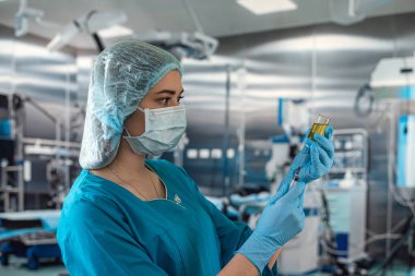 Tıbbi olarak sterilize edilmiş üniformalı güzel bir kadın cerrah ameliyathanede bir hastaya uygulanacak bir şırıngayı elinde tutuyor. İlaç. Doktor. Ellerinde şırınga