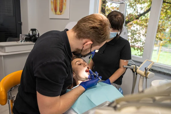 Treatment of a carious tooth in the office of a dental clinic. The dentist performs teeth cleaning and root canal treatment and filling. the assistant sterilizes the mouth with a saliva aspirator.