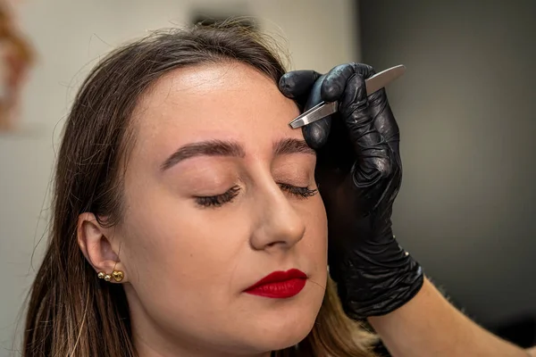 Close-up of a young woman during an eyebrow correction procedure in a beauty salon. tweezers. eyebrow epilation